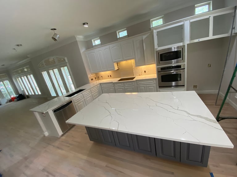 Modern kitchen with white cabinetry, large marble island, stainless steel appliances, and natural lighting from windows