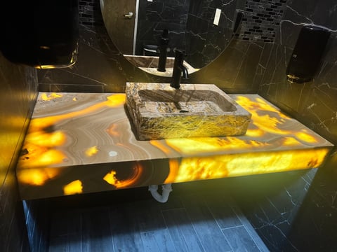 Modern sink with golden yellow marble countertop featuring swirled pattern and rectangular stone basin under overhead mirror lighting