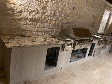 Unfinished outdoor kitchen with granite countertop, stainless steel grill, and stone brick walls under construction