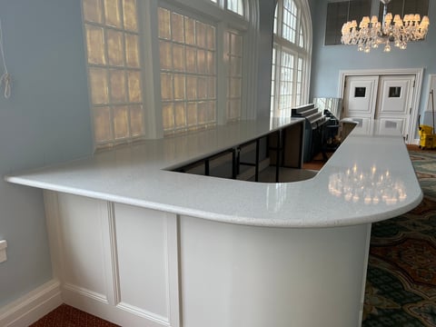 Modern white curved reception desk with light countertop in bright office interior with chandelier and tall windows
