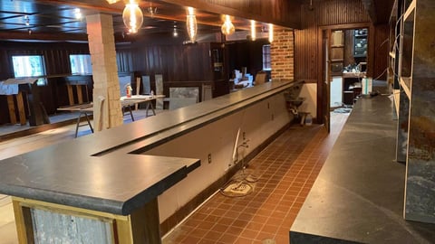 Empty restaurant bar with long counter, brick walls, pendant lighting, and terracotta floor
