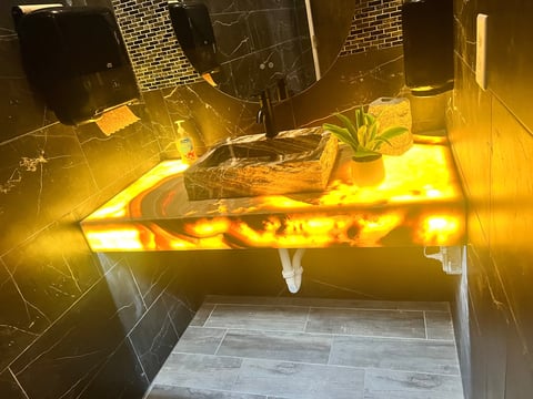 Modern bathroom vanity with glowing yellow LED lighting underneath, featuring a dark vessel sink, potted plant, and minimalist design