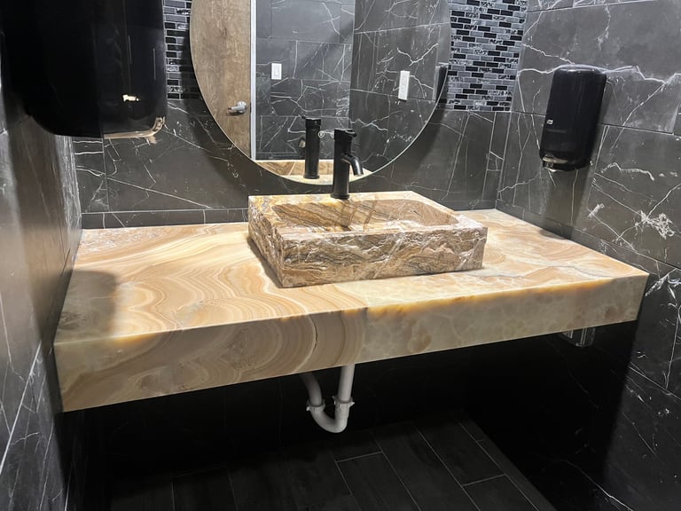 Modern bathroom vanity with natural stone basin sink and marble countertop, black marble tile backsplash, and round mirror with fixtures