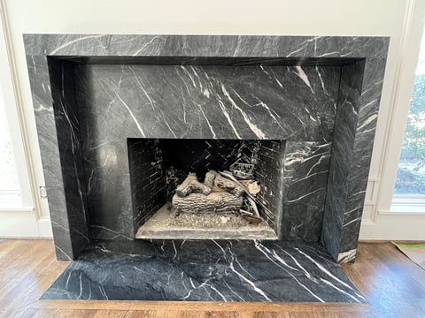 Modern fireplace with dark marble surround and arched opening, empty firebox visible, wooden floor and white walls in background