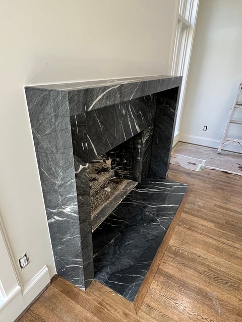 Modern fireplace with dark marble surround and hearth, under construction in a room with wooden flooring and cream walls