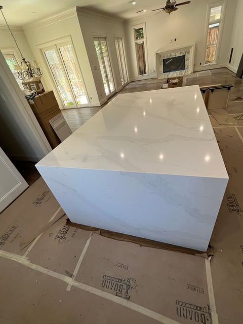 Large white marble island countertop installed in a bright, open kitchen with white cabinetry and hardwood flooring