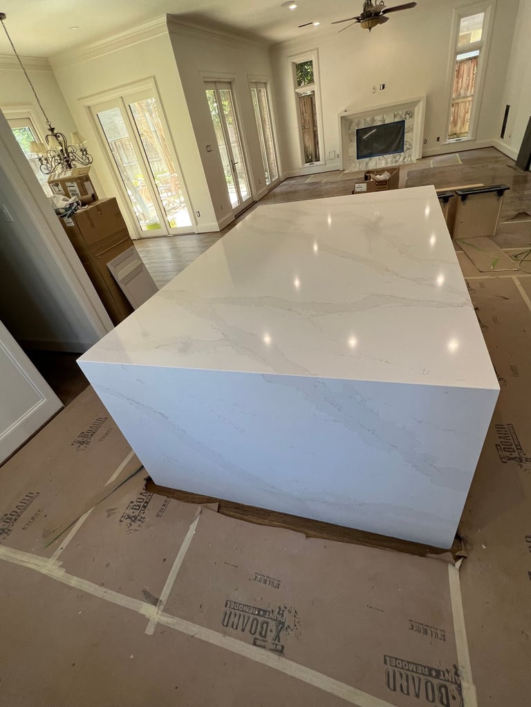 Large white marble island countertop installed in a bright, open kitchen with white cabinetry and hardwood flooring